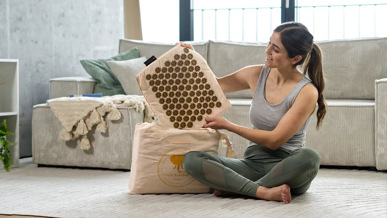 Eine Frau sitzt auf dem Boden und hält eine Akupressurmatte in der Hand | CALM ELEPHANT Akupressurmatten aus nachhaltiger Produktion und natürlichen Materialien